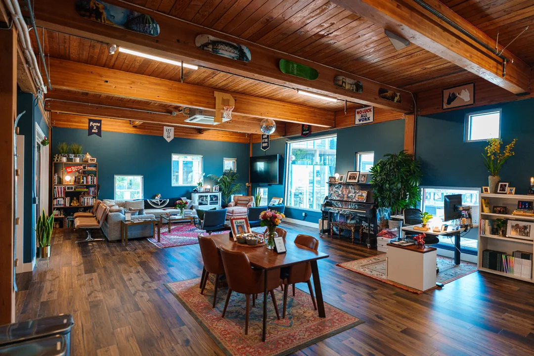 TEDxPortland HQ: open-plan lounge with a dining table, sofas and shelving under an exposed timber ceiling