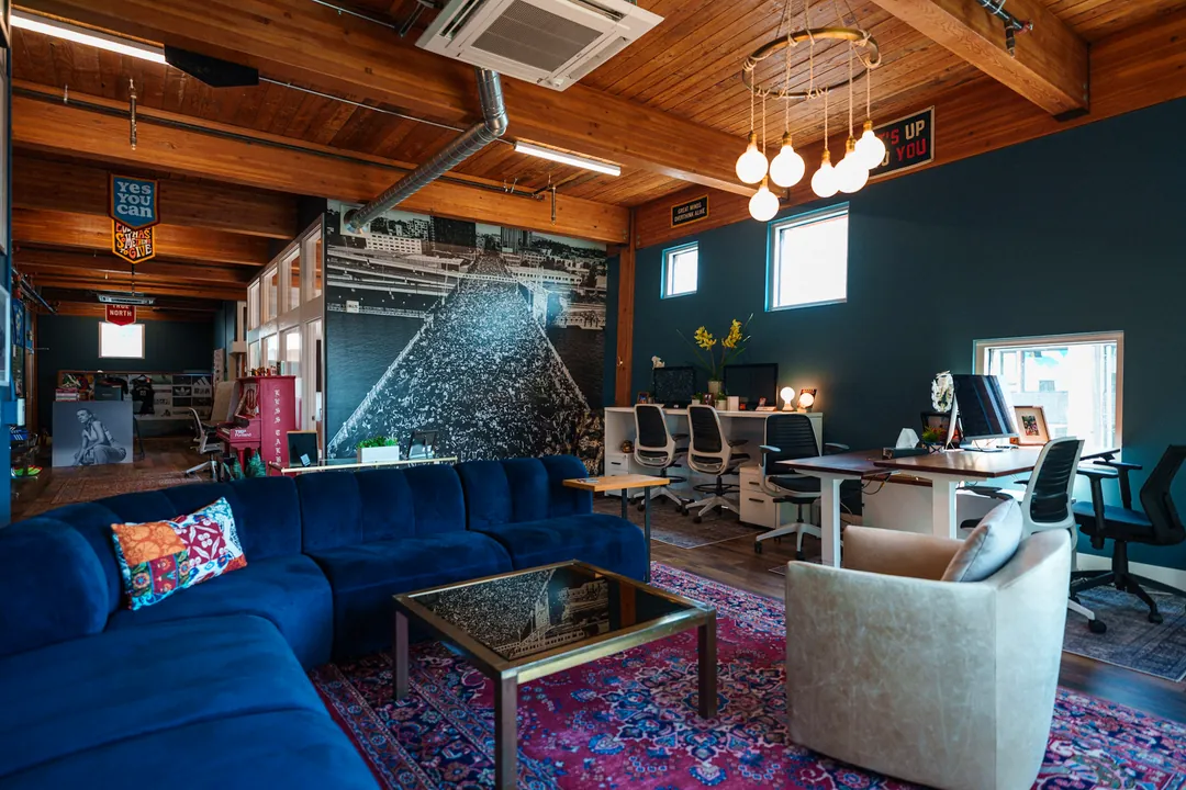 TEDxPortland HQ: navy sectional and glass coffee table under a pendant light, desks beyond