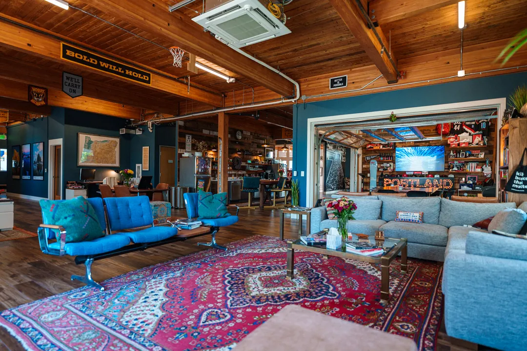 TEDxPortland HQ: blue armchairs and a sectional sofa on a red rug, the PORTLAND sign in the background